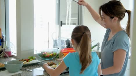 woman with her daughter keeping noddle on plate in kitchen 4k