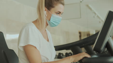 junge sportliche frau mit gesichtsmaske benutzt ein trainingsgerät im fitnessstudio