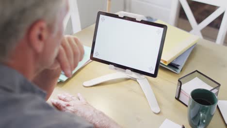 Caucasian-man-sitting-at-table-in-kitchen,-using-tablet-with-copyspace