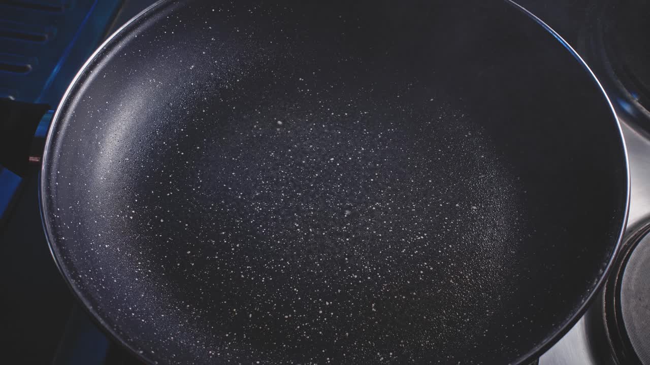 rociando aceite en una sartén, preparándose para cocinar en la cocina de casa