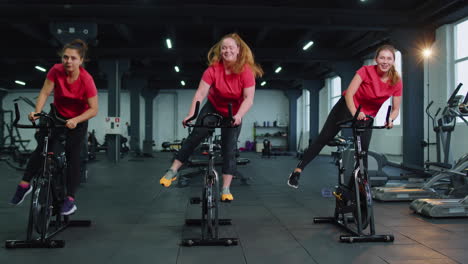 Grupo-De-Mujeres-Atléticas-Montando-En-Rutina-De-Entrenamiento-De-Bicicleta-Estacionaria-Giratoria-En-El-Gimnasio,-Pérdida-De-Peso-En-Interiores