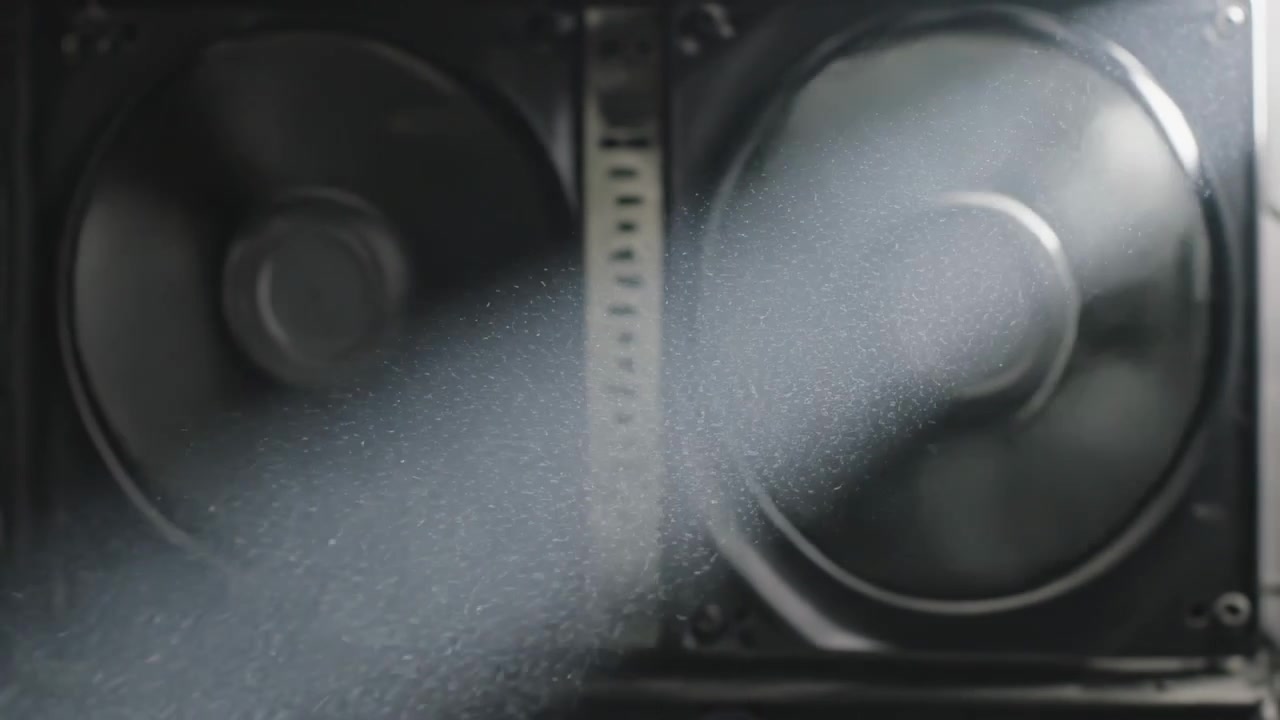 Spinning two axial cooling fans rotating inside electronics chassis, diagonal light revealing dust