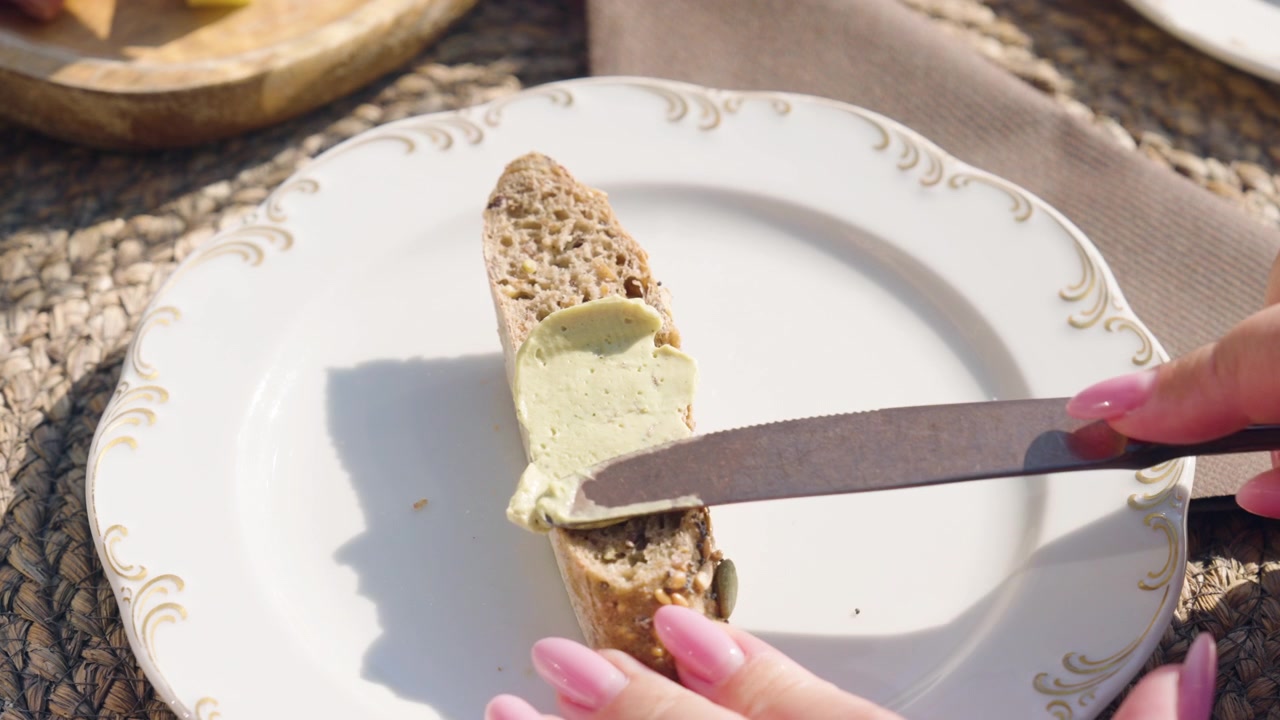 Cropped Hand Spreads Cream Onto A Slice Of Bread While Eating Outdoors During A Vacation. Close-up Shot
