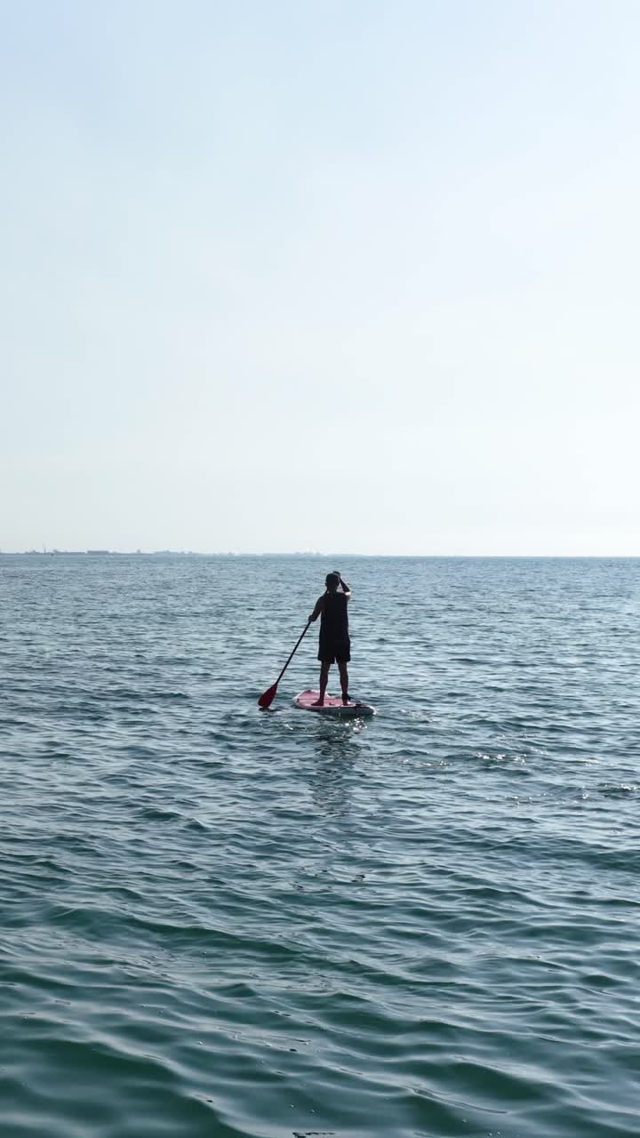 Man paddle boarding on calm ocean water. Vertical