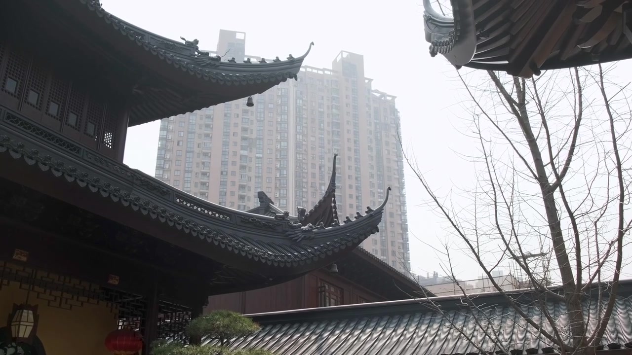 Tetti di templi tradizionali cinesi con grondaie curve e ornate contrastano con i moderni grattacieli in un paesaggio urbano nebbioso di Shanghai.