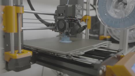 Dolly-in-shot-on,-3D-printer-which-printing-blue-sprocket-in-white-laboratory