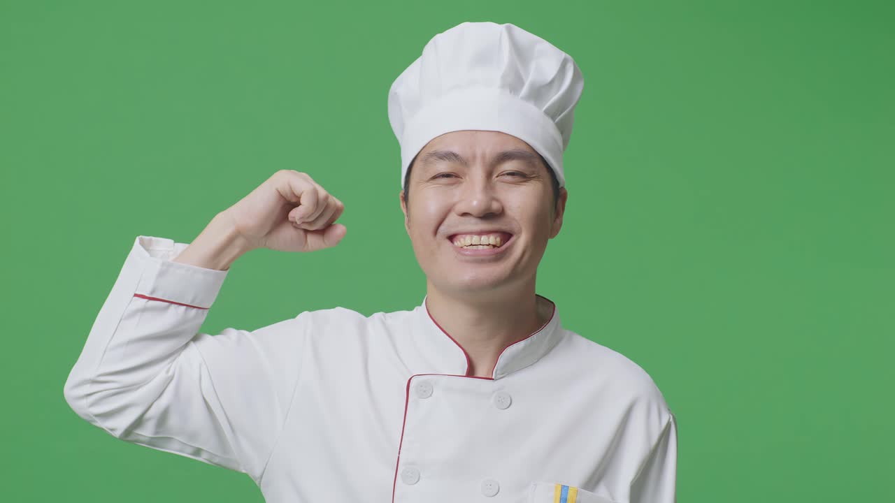 Close Up Of Asian Man Chef Smiling And Flexing His Bicep While Standing In The Green Screen Background Studio