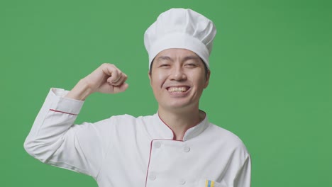 Close Up Of Asian Man Chef Smiling And Flexing His Bicep While Standing In The Green Screen Background Studio
