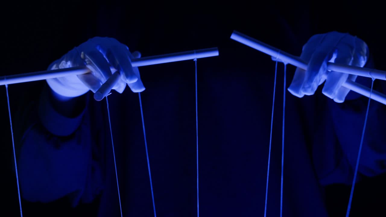Hands in White Gloves Manipulating Puppet Strings in Blue Light