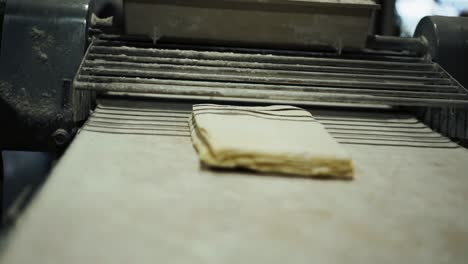 medium shot of slab roller croissant dough machine rolling sheets of laminated croissant dough, focus pulling from machine to pastry