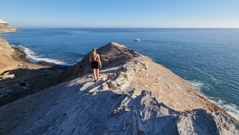 young-woman-walks-on-the-slope-of-the-mountains-located-near-the-beach-of-Medio-Almud-on-the-island-of-Gran-Canaria-and-on-a-sunny-day