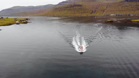 aerial of boat sailing in the dark water in a fjord surrounded by beautiful landscape of mountains on the faroe islands