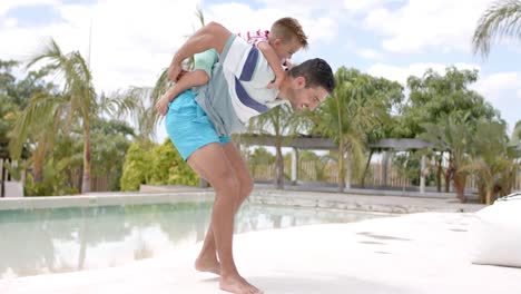 Happy-caucasian-father-carrying-his-son-at-swimming-pool-at-beach-house