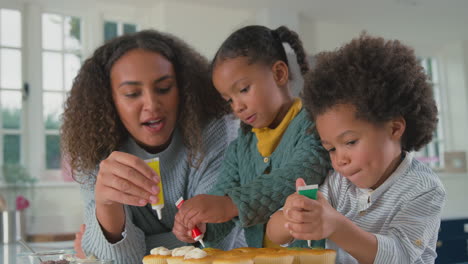 mother with children in kitchen decorating cupcakes together