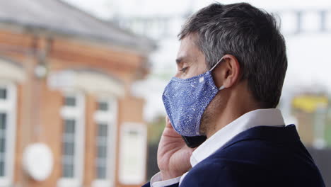 businessman on railway platform talking on mobile phone wearing ppe face mask during health pandemic