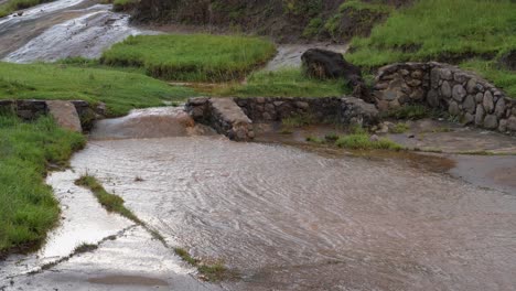 Muddy-river-water-floods-across-concrete-culvert-on-rural-road