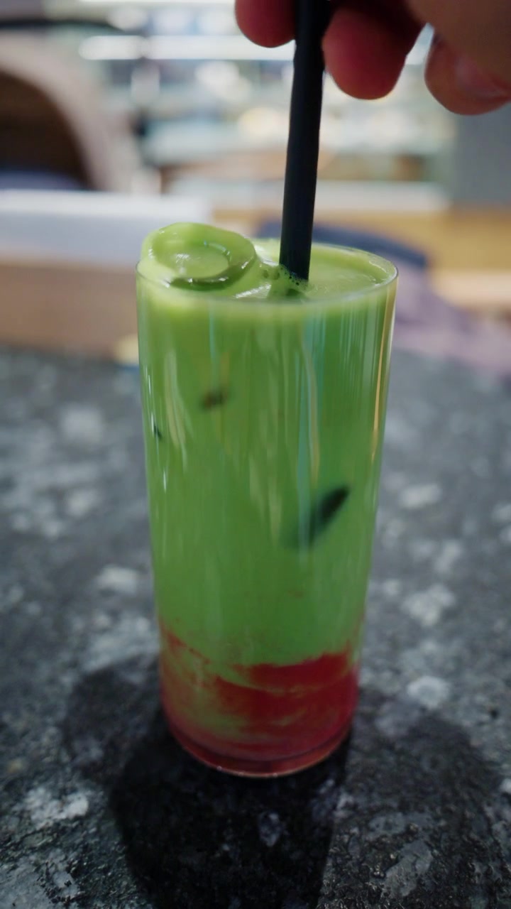 Primo piano di una bevanda verde colorata con una cannuccia nera su un tavolo da caffè.