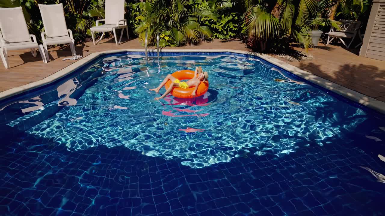 Aerial view of a person relaxing on an orange float in a pool, capturing summer vibes