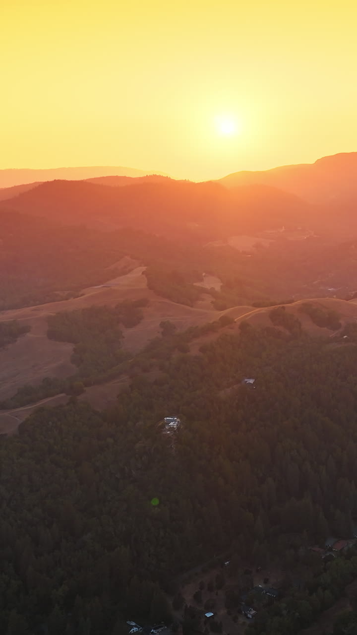 Sunlit mountainous landscape at sunset. Beautiful silhouettes of mountains at the backdrop of orange sky. Top view. Vertical video