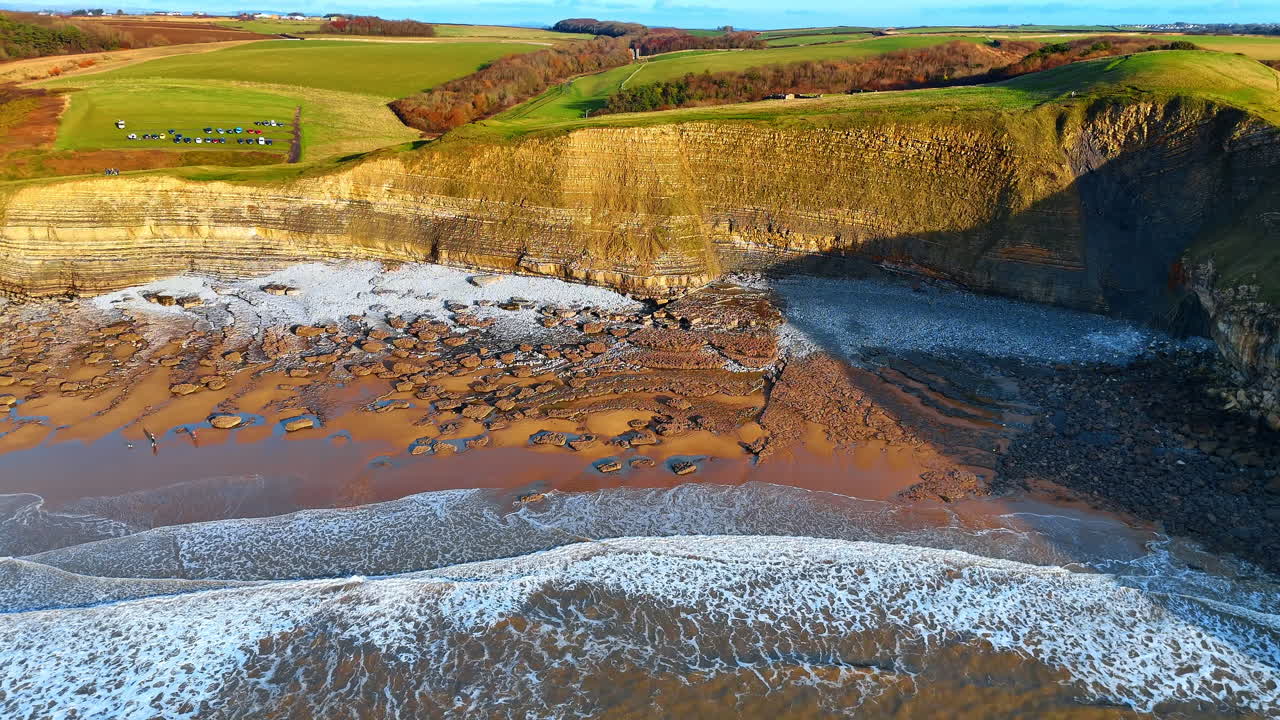 Aerial view of stratified limestone cliffs and rocky beach. Direct drone shot showing geological layers of cliffs and a pebble beach with scattered rocks at low tide