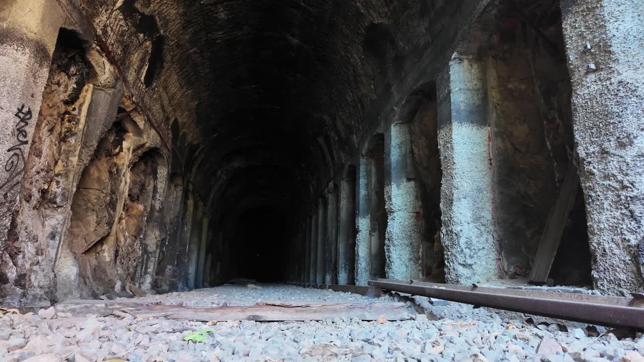Drone voando baixo através de um túnel de concreto escuro e abandonado com pilares e paredes em decomposição. Tomada cinematográfica de exploração capturando uma atmosfera subterrânea misteriosa e um ambiente de exploração urbana.