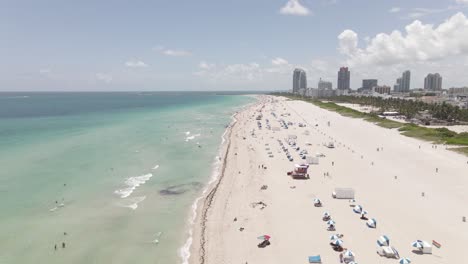Low-aerial-flyover-people-enjoying-sunny,-sandy-South-Beach-Miami