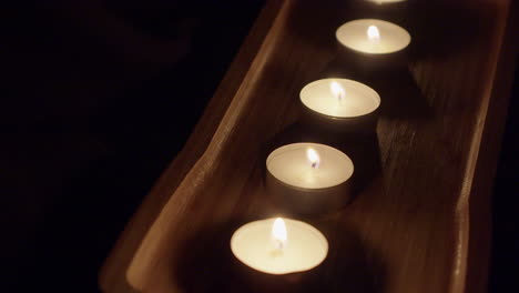 Dark-moody-background:-Tea-candles-burn-in-decorative-wooden-tray