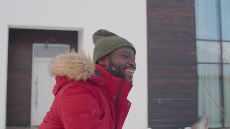 joyous african american man playing snowballs outside