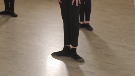 a group of young ballet students in black dancewear practicing positions in a spacious ballet studio with wooden flooring and wall-mounted barres. focused expressions and synchronized movements.