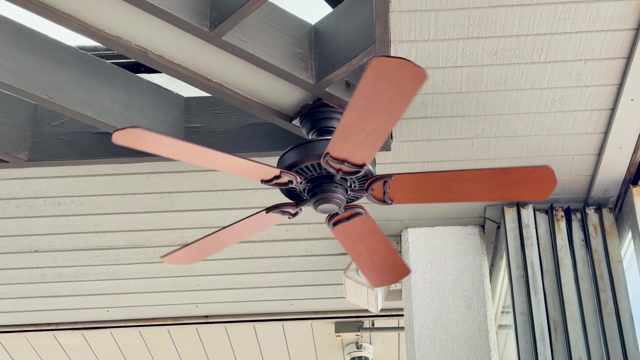Tomada estática de baixo ângulo de um ventilador de teto de madeira girando em um pátio coberto.