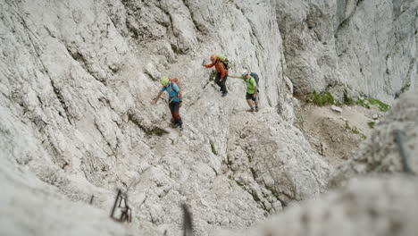 excursionistas escalando una parte empinada de una escalada en colores brillantes usando cascos y mochilas