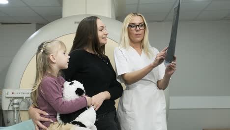 mujer radióloga explica los resultados de la resonancia magnética para una mujer con su hijo, mostrando la instantánea con imágenes, observando y analizando la resonancia eléctrica en una clínica moderna junto con la mri de tipo cerrado moderna