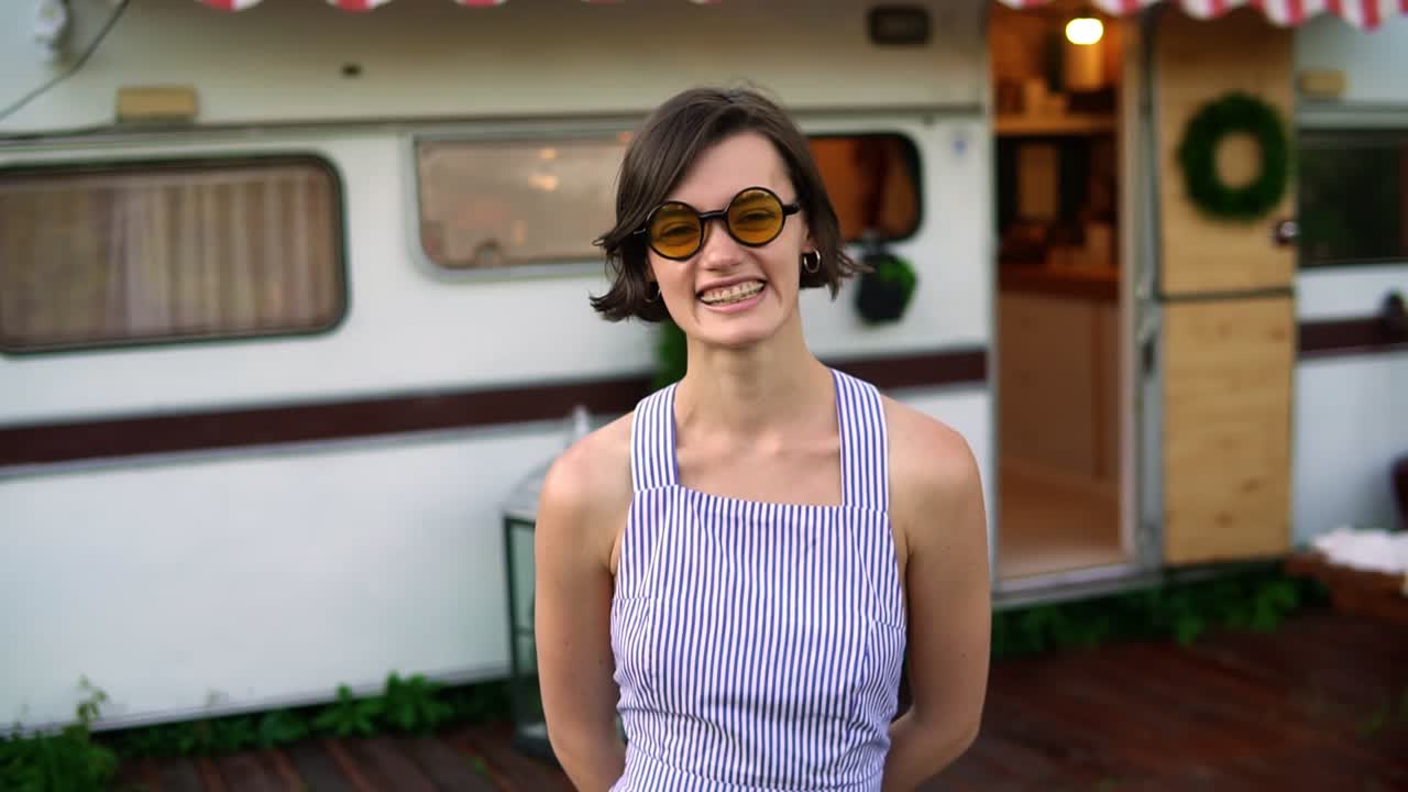 hermosa morena con un vestido azul de verano y elegantes sungrasses se ríe de pie con el remolque en el fondo