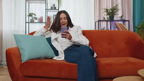 Happy-lovely-girl-at-home-couch-use-smartphone-typing-browsing-say-wow-yes-found-out-great-big-win