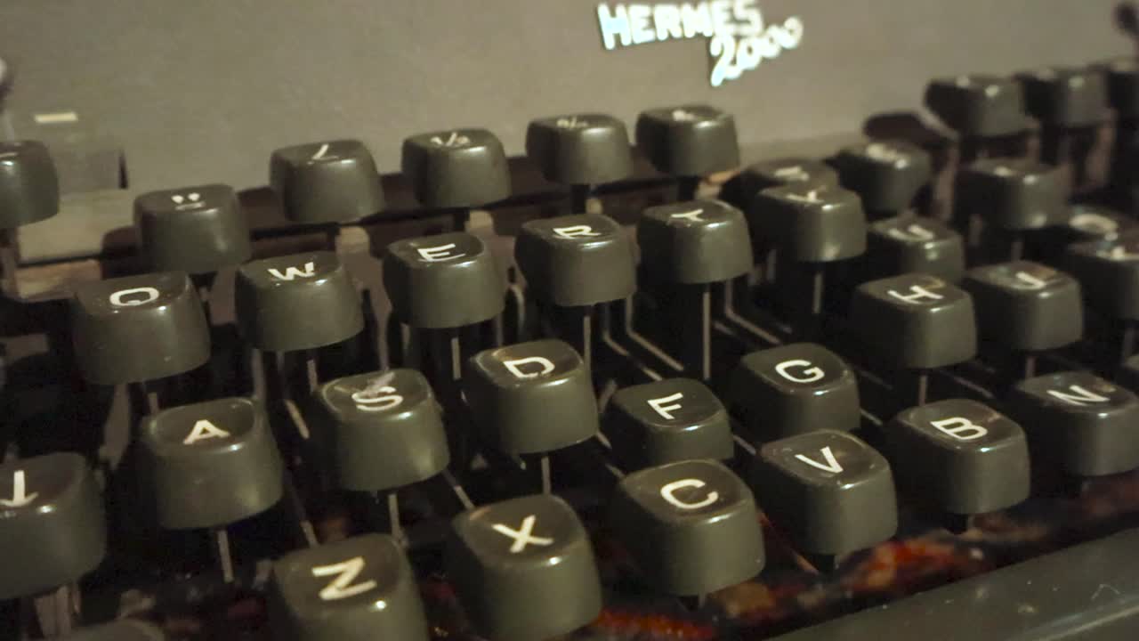 Old gray and vintage awesome looking typewriter called Hermes 2000 close up footage while the footage glides over it from left to right. Retro keyboard in sharp focus with buttons slightly dusty.
