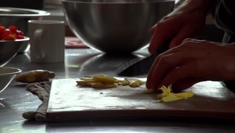 a cook slices strands of fresh ginger root in preparation for a restaurant dish