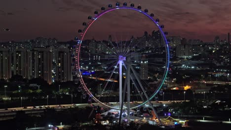 orbital aerial view of cantilever observation wheel at night in saint paul, brazil. clear sky, lights, buildings, skyline, landscape. roda rico.
