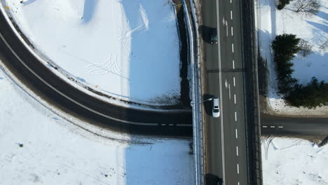 Cars-driving-over-a-viaduct-crossing-another-curved-black-road-and-between-the-trees-on-a-winter-landscape