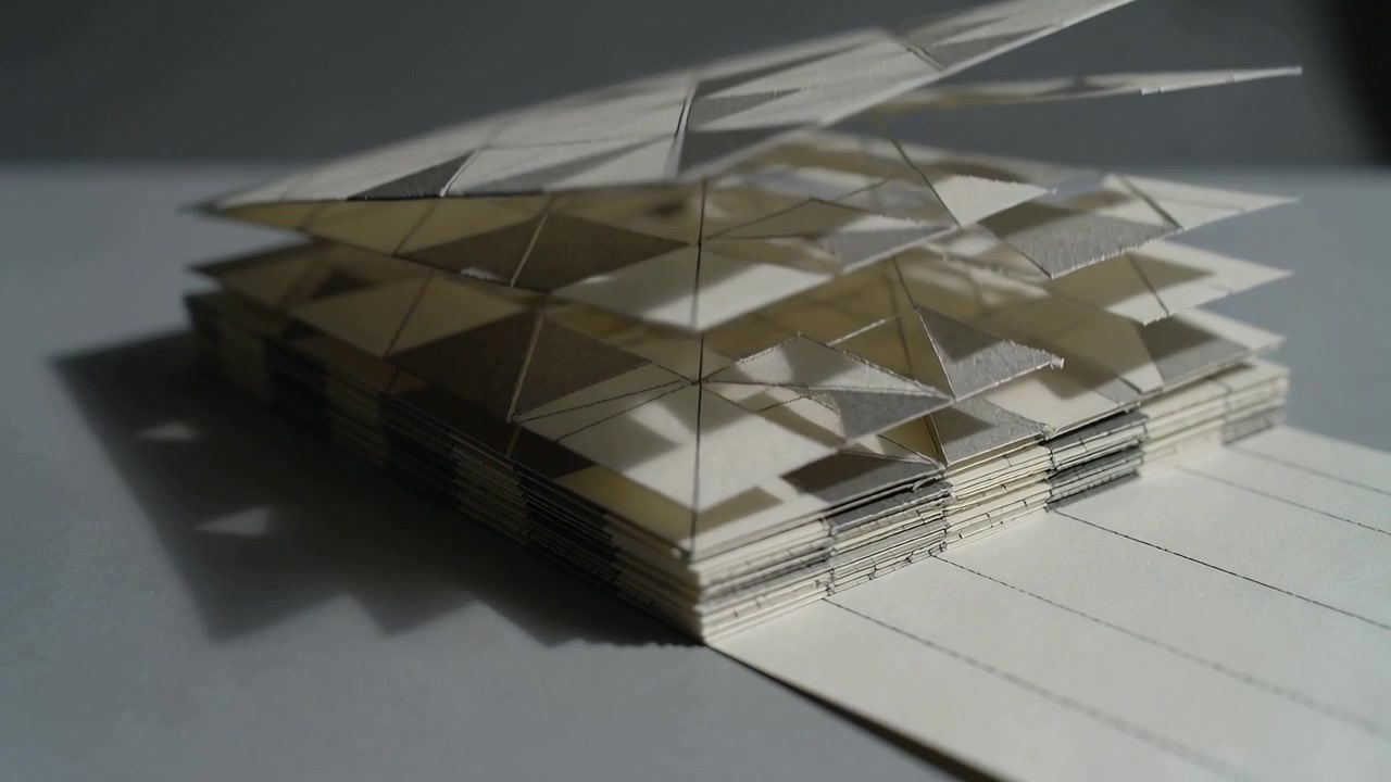 Pulling lined tab, paper pop-up assembly lifting triangle panels on tabletop, casting shadow layers