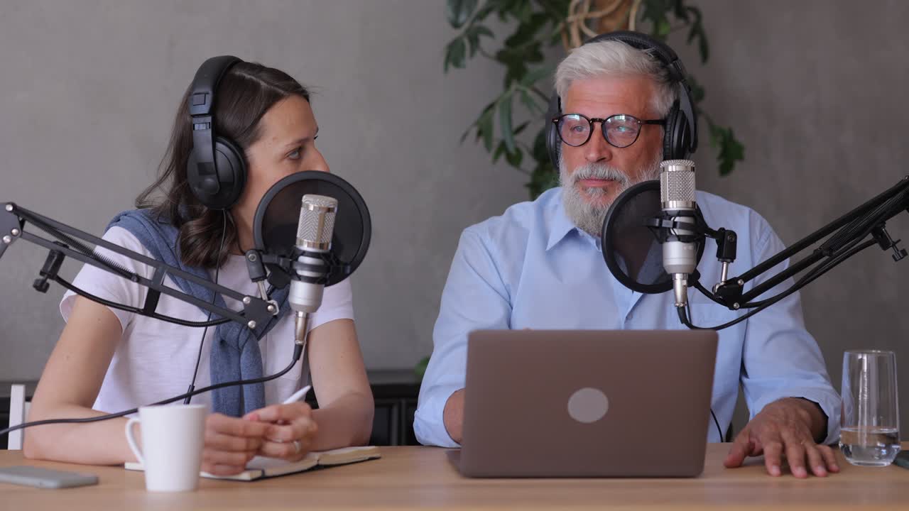 un hombre y una mujer graban un podcast o una entrevista con un micrófono en un estudio de grabación. un hombre adulto de cabello gris y una joven europea crean contenido de audio, graban anuncios y libros de audio