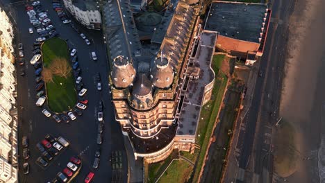 Toma-Aérea-Superior-Del-Gran-Hotel-Con-Algunos-Vehículos-Estacionados-En-La-Carretera-Al-Lado-Durante-Un-Día-Soleado-En-Scarborough-North-Yorkshire,-Inglaterra