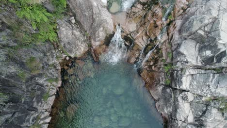 Arriba-Hacia-Abajo-Lentamente-Incline-Hacia-Arriba-La-Piscina-Natural-Esmeralda-A-Través-De-Una-Pequeña-Cascada,-Portela-Do-Homem---Gerês