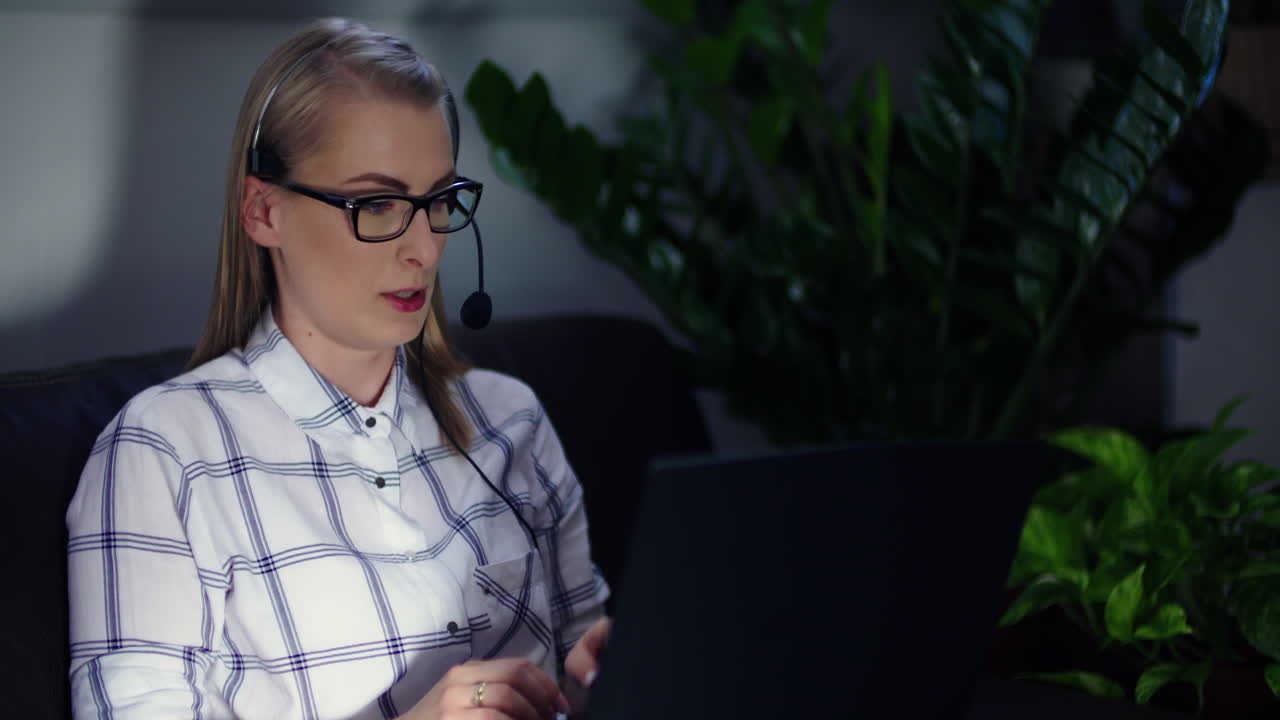 Confident Female Office Worker Talking On Headset While Using Laptop On Sofa At Office