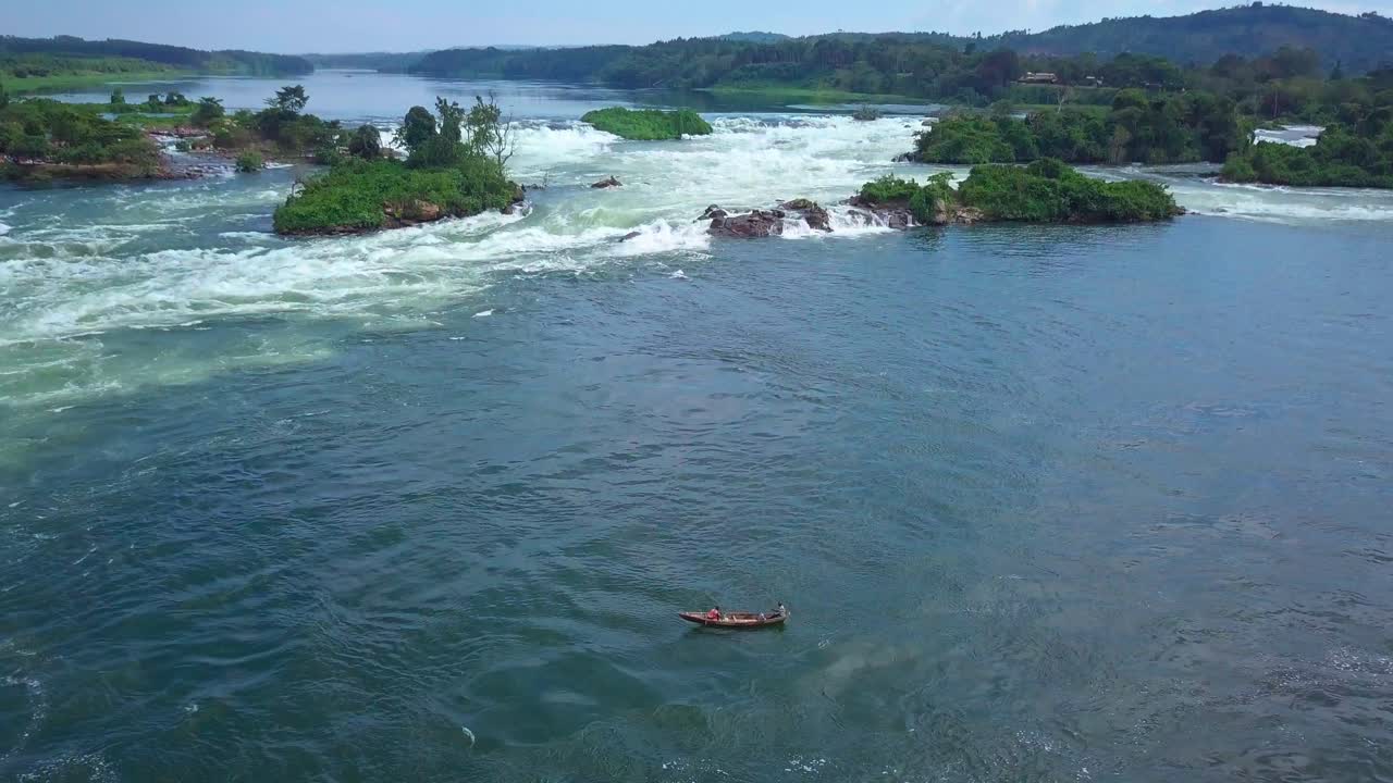 Aerial view capturing a fisherman sailing on the River Nile in Uganda, navigating through rapids and rocky terrain under a bright, sunny sky, showcasing the beauty of nature, drone establishing shot
