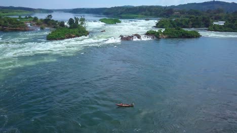 aerial view capturing a fisherman sailing on the river nile in uganda, navigating through rapids and rocky terrain under a bright, sunny sky, showcasing the beauty of nature, drone establishing shot