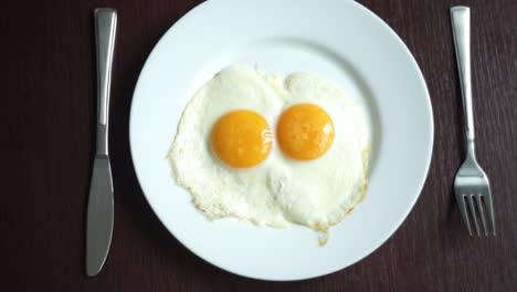 fried eggs on plate. putting plate with fried eggs on wooden table