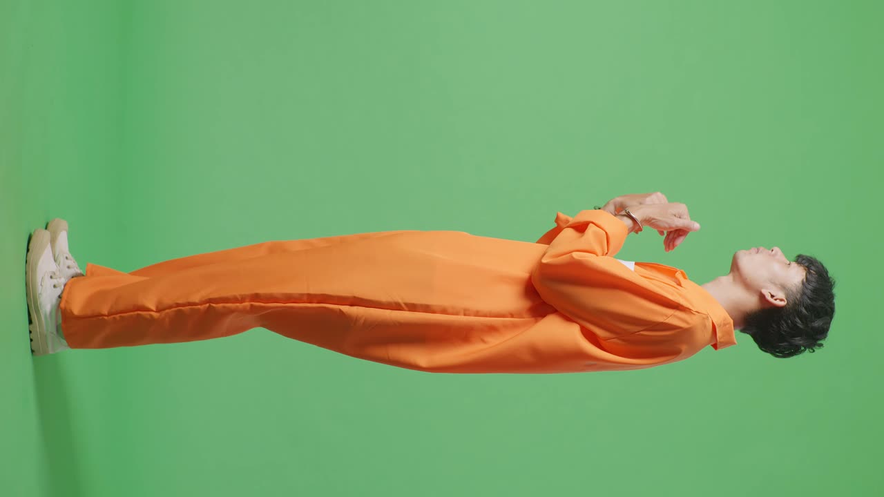 손을 은 아시아 남성 수감자가 초록색 스크린 배경에서 의심스럽게 서서 화를 내며 손을 들고 "왜?"라고 외치고 있습니다.