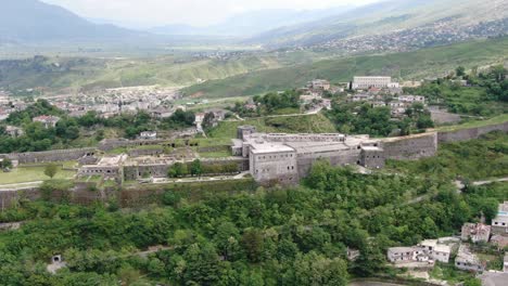 Drone-view-in-Albania-flying-in-Gjirokaster-town-over-a-medieval-castle-on-high-ground-fort-showing-the-brick-brown-roof-houses