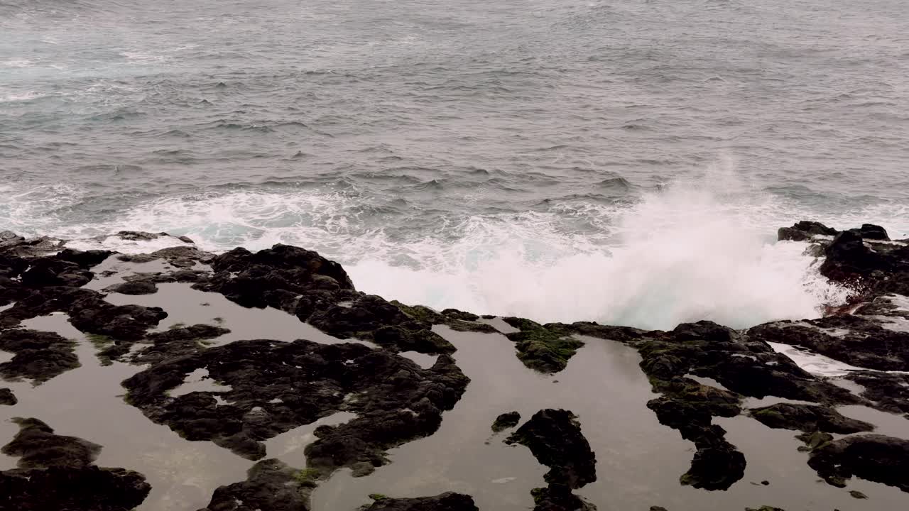 Le onde dell'oceano si infrangono sulle scogliere vulcaniche scure della costa dell'isola di São Miguel, Azzorre, Portogallo.