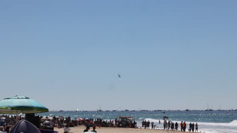 crowded beach scene with helicopter flying over ocean